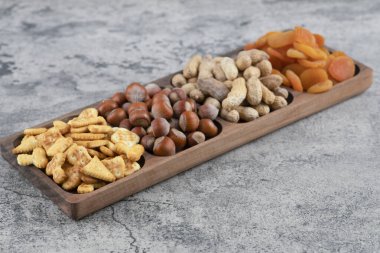 Tahta tabak dolusu fındık, kraker ve mermer yüzeyde kurutulmuş kayısı. Yüksek kalite fotoğraf