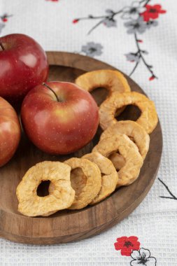 Ahşap bir tabak kırmızı elma ve masa örtüsünün üzerinde kurumuş halkalar. Yüksek kalite fotoğraf
