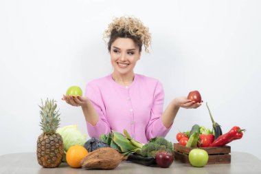 Kıvırcık kadın bir sürü taze sebzeyle masada oturuyor.