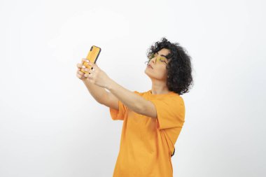 Sarı tişörtlü esmer kıvırcık kadın akıllı telefondan selfie çekiyor. Yüksek kalite fotoğraf