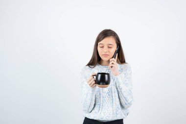 Elinde bir fincan sıcak kahve tutan ve telefonda konuşan genç bir kadın. Yüksek kalite fotoğraf