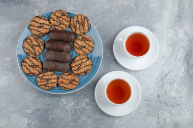Mavi tabak dolusu çikolatalı kek ve bir fincan sıcak çayla kepekli kurabiye. Yüksek kalite fotoğraf