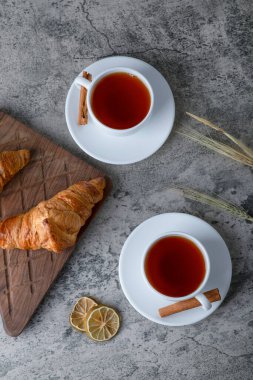 Tahta kesme tahtası, taze kruvasan ve taştan bir arka fona yerleştirilmiş beyaz fincan sıcak çay. Yüksek kalite fotoğraf