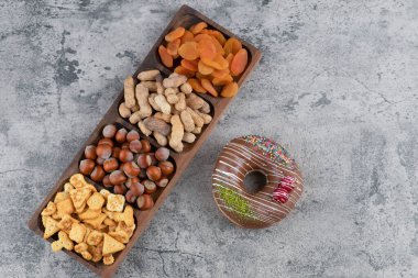 Tahta tabak dolusu fındık, kraker ve mermer yüzeyde çikolatalı çörekle kurutulmuş kayısı. Yüksek kalite fotoğraf