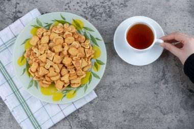 Kadın eli mermer arka planda krakerlerin yanında sıcak çay bardağını tutuyor. Yüksek kalite fotoğraf