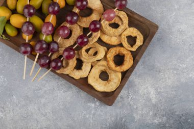Kurumuş elma halkaları, kumkatlar ve mermer zemin üzerinde kırmızı üzümlerle dolu ahşap bir tabak. Yüksek kalite fotoğraf