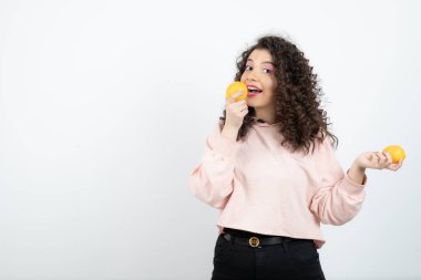 Pembe kazaklı, portakal yiyen kıvırcık kadın portresi. Yüksek kalite fotoğraf