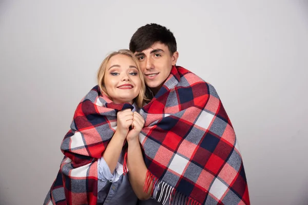 美しい若いカップルは灰色の背景に暖かい毛布に包まれています 高品質の写真 — ストック写真