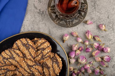 Siyah bir tabak tatlı bisküvi, bir bardak çay ve masada kurumuş güller. Yüksek kalite fotoğraf