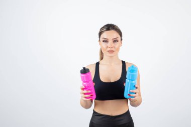 Mavi ve pembe su şişeleri tutan genç atletik kadın portresi. Yüksek kalite fotoğraf