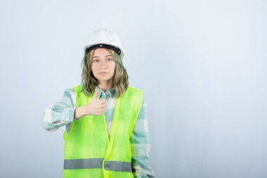 Beyaz şapkalı, ayakta duran ve baş parmak kaldıran genç bir inşaat işçisi resmi. Yüksek kalite fotoğraf