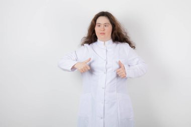 Aşağı sendromlu genç bir kız modelin portresi ayakta ve baş parmağını kaldırıyor. Yüksek kalite fotoğraf