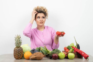 Kıvırcık kadın bir sürü taze sebzeyle masada oturuyor.