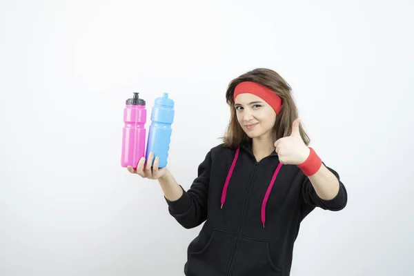 Beautiful Sporty Woman Holding Colorful Bottles Showing Thumb High Quality — Stock Photo, Image