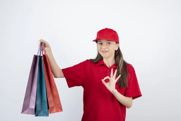 Obraz Młodej Nastolatki Czerwonym Mundurze Pokazujący Gest Trzymającej Torby Zakupy — Zdjęcie stockowe
