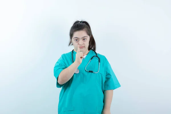白い壁にカメラに指を指差して聴診器を持つ若い女性看護師 高品質の写真 — ストック写真