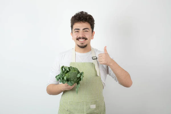 Sonriente Jovencito Haciendo Gestos Con Pulgar Hacia Arriba Sosteniendo Brócoli —  Fotos de Stock