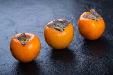 Siyah yüzeye yerleştirilmiş üç taze fuyu hurması. Yüksek kalite fotoğraf