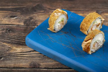 Tahta kesme tahtasına yerleştirilmiş taze, lezzetli suşi ruloları, karides ve zencefil dilimleri. Yüksek kalite fotoğraf