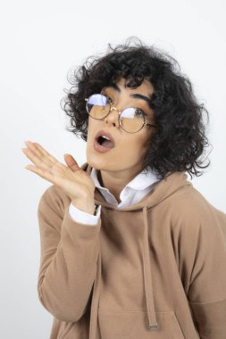 Kıvırcık saçlı, gözlüklü esmer kadın, beyazın üstünde mutlu bir yüz yapıyor. Yüksek kalite fotoğraf