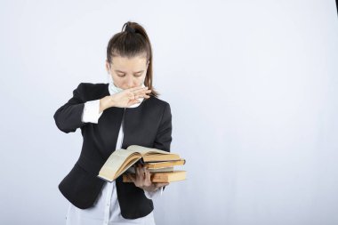Genç bir kız öğrenci elinde kitaplarla beyaz duvarın üzerinde ağzını kapatıyor. Yüksek kalite fotoğraf