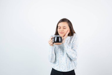 Beyaz bir duvarın üzerinde elinde bir fincan sıcak kahve tutan genç bir kadın. Yüksek kalite fotoğraf