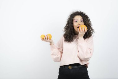 Pembe kazaklı, portakal yiyen kıvırcık kadın portresi. Yüksek kalite fotoğraf
