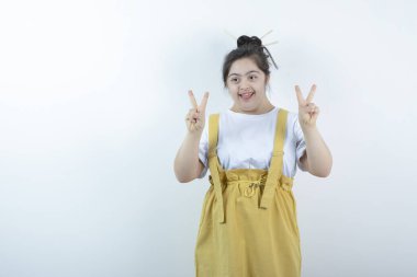 Genç ve güzel kız model ayakta duruyor ve beyaz duvara karşı zafer işareti gösteriyor. Yüksek kalite fotoğraf