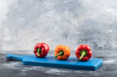 Three fresh organic colorful bell peppers on blue cutting board. High quality photo