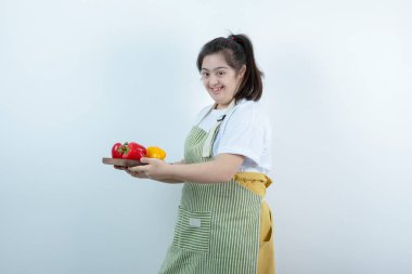 Önlüklü genç bir kız taze sebzeli ahşap bir tahta taşıyor. Yüksek kalite fotoğraf