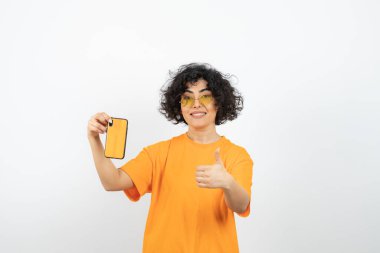 Esmer kıvırcık kadın cep telefonu tutuyor ve parmağını kaldırıyor. Yüksek kalite fotoğraf