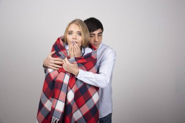 Genç adam, donan kız arkadaşını ekose battaniyeyle örterken gri duvarda dikiliyor. Yüksek kalite fotoğraf