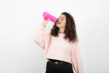 Süveter giyen genç kıvırcık kadın doğrudan şişeden su içiyor. Yüksek kalite fotoğraf