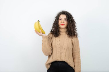 Beyazın üzerinde muz tutan kıvırcık bir genç kadının fotoğrafı. Yüksek kalite fotoğraf