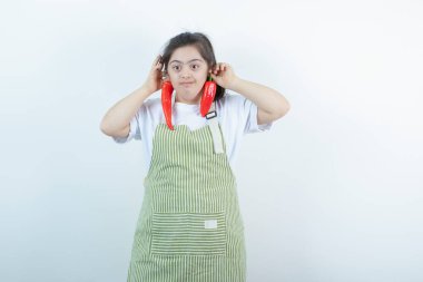 Kareli önlüğün içinde duran ve elinde iki kırmızı acı biber tutan genç ve güzel bir kız. Yüksek kalite fotoğraf