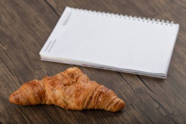 Tahta masaya beyaz defter konmuş lezzetli tereyağlı kruvasan. Yüksek kalite fotoğraf