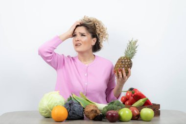 Genç bayan model ananas elinde, masada meyve dolu oturuyor. Yüksek kalite fotoğraf