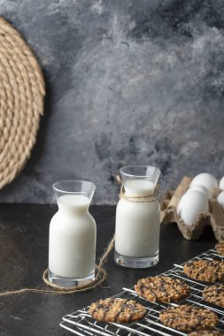 Siyah arka planda taze susamlı kurabiye olan iki süt şişesinin dikey fotoğrafı. Yüksek kalite fotoğraf