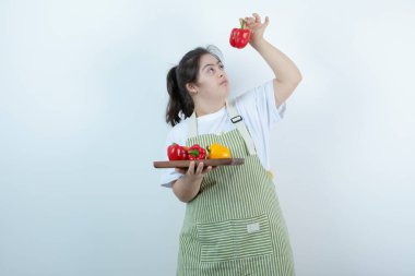 Önlüklü genç bir kız elinde taze sebzelerle tahta bir tahta tutuyor. Yüksek kalite fotoğraf