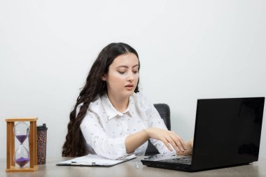 Genç bayan çalışan, dalgalı saçlı masada oturuyor ve laptopunu arıyor. Yüksek kalite fotoğraf