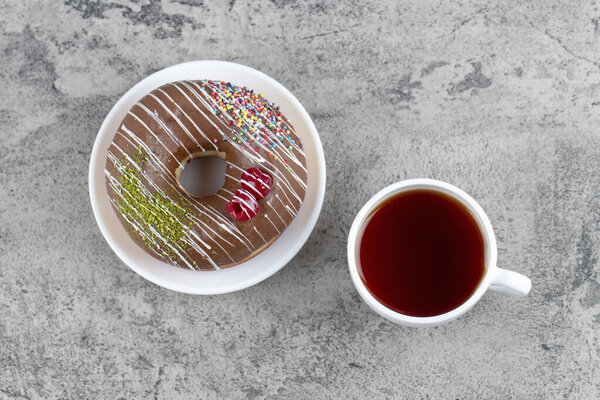 Chocolate donut with berries and sprinkles and cup of hot tea on stone background. High quality photo