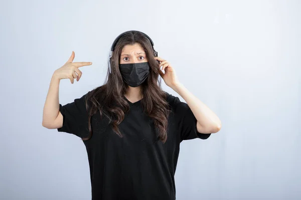 ヘッドフォンを指す医療用マスクの長い髪を持つブルネットの女性 高品質の写真 — ストック写真