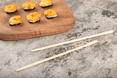 Taş bir masanın üzerine karides ve çubuklarla taze lezzetli suşi ruloları. Yüksek kalite fotoğraf