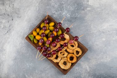 Kurumuş elma halkaları, kumkatlar ve mermer zemin üzerinde kırmızı üzümlerle dolu ahşap bir tabak. Yüksek kalite fotoğraf