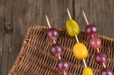 Ahşap arka planda sepetin üzerine sopa yapıştırılmış Kumquat ve üzüm parçaları. Yüksek kalite fotoğraf