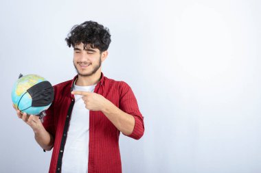 Genç adam, tıbbi maskeli bir toprak küresini işaret ediyor. Yüksek kalite fotoğraf
