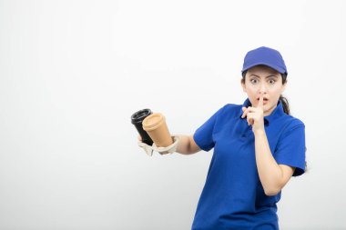 Mavi üniformalı, elinde bardakları olan süpriz bir kadın sessiz bir işaret gösteriyor. Yüksek kalite fotoğraf