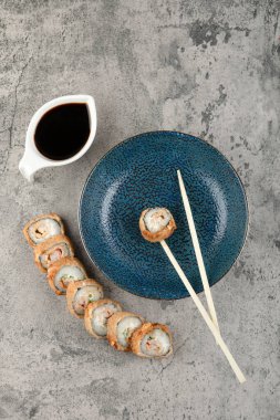 Mavi tabak, sıcak suşi ruloları ve taş yüzeyde soya sosu. Yüksek kalite fotoğraf