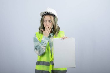 Güzel bayan mühendisin boş tuval tutarken ve ağzını kapatırken çekilmiş bir fotoğrafı. Yüksek kalite fotoğraf