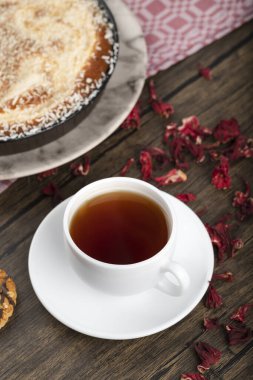 Hindistan cevizi parçalı bir tabak tatlı turta, gül yaprakları ve ahşap arka planda bir fincan çay. Yüksek kalite fotoğraf